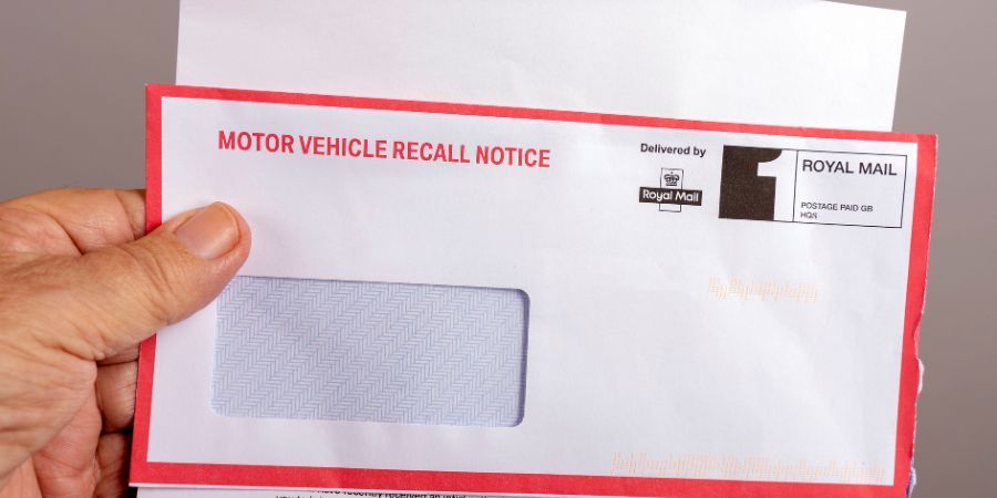 Hand holding a motor vehicle recall notice envelope delivered by Royal Mail.