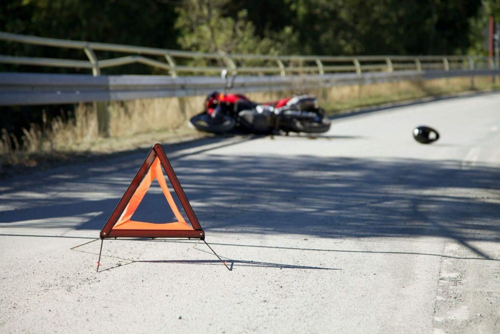 a triangle sign sitting on the side of a road next to a motorcycle
