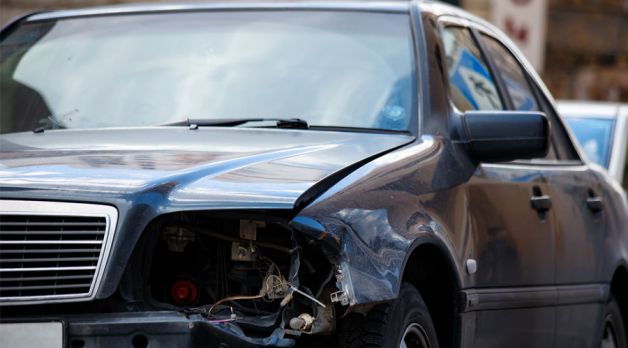 Damaged car with broken headlight and dented fender on street, showing vehicle accident aftermath.