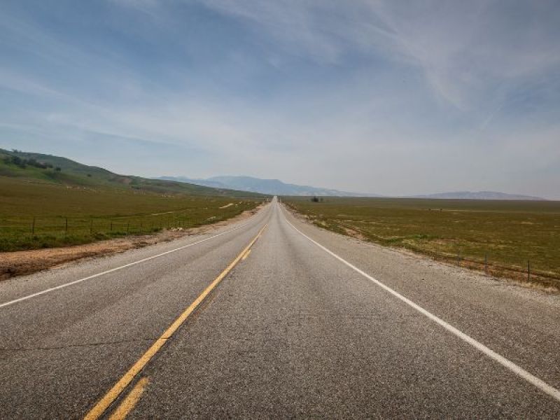 Open road stretching into horizon under blue sky, flanked by green fields, conveying freedom and adventure.