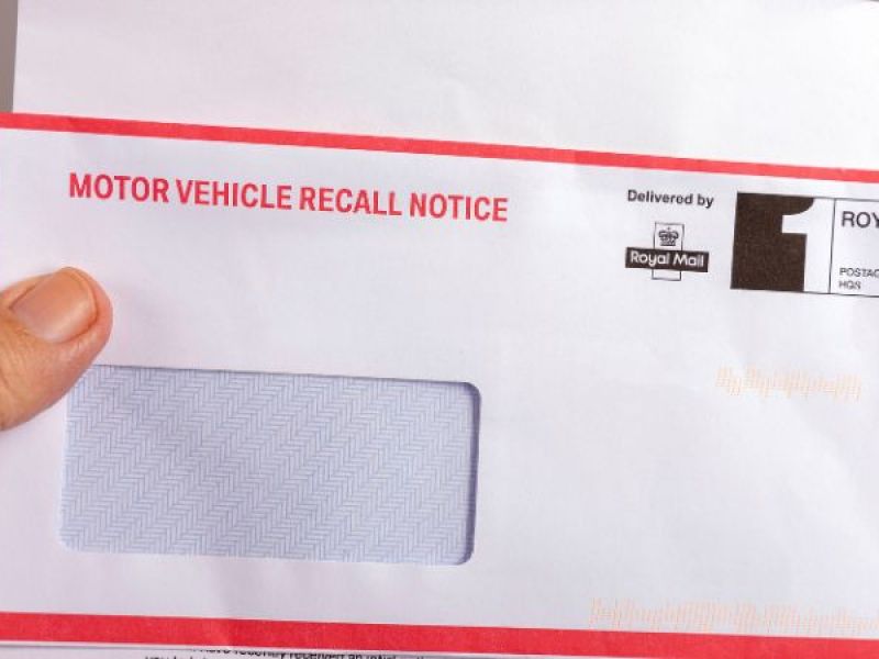 Hand holding a motor vehicle recall notice envelope delivered by Royal Mail.