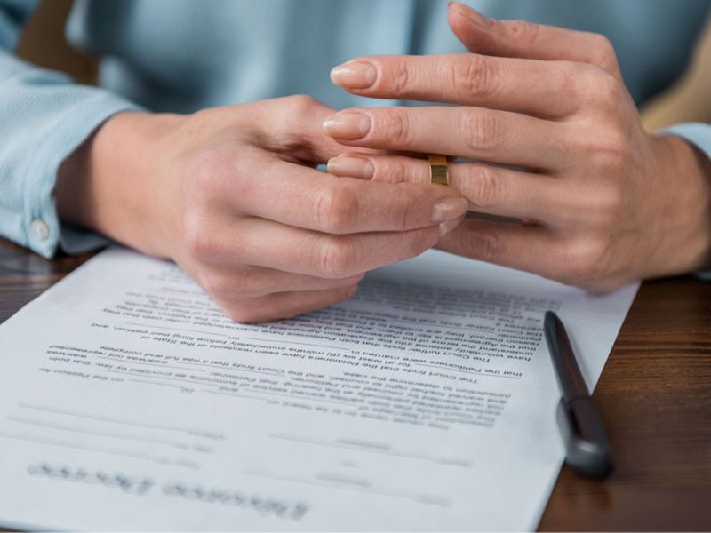 woman taking off wedding ring and divorce decree on table