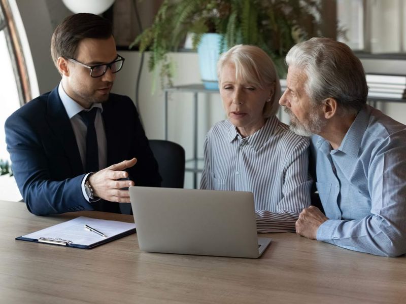 Financial advisor explaining investment options to a senior couple using a laptop in an office setting.