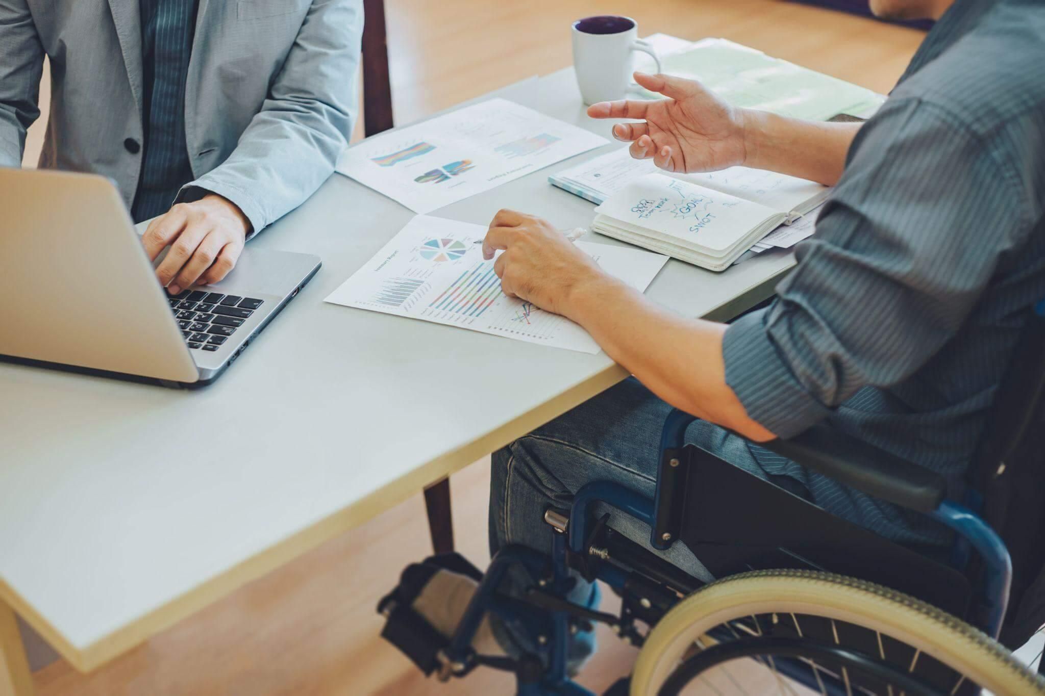 Two men discussing disability benefits with laptops and papers