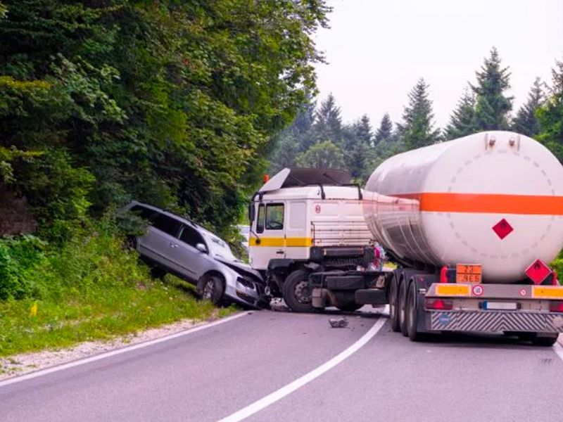 Truck and car accident on a curved road with trees in the background.