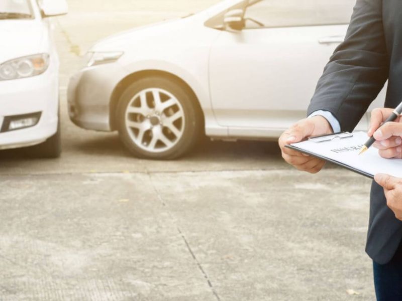 Two people in formal attire are standing and reading a legal document, two cars in the background are parked after what seems like an accident