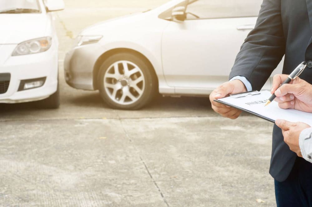 Two people in formal attire are standing and reading a legal document, two cars in the background are parked after what seems like an accident