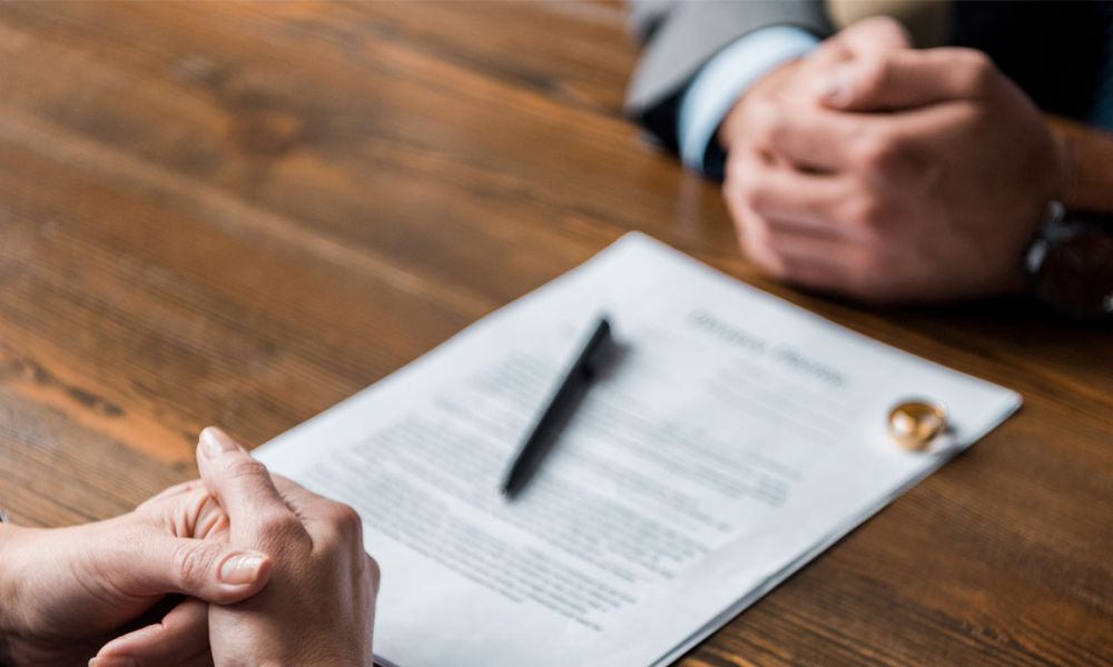 partial view of lawyer and client sitting at table with divorce decree and wedding rings