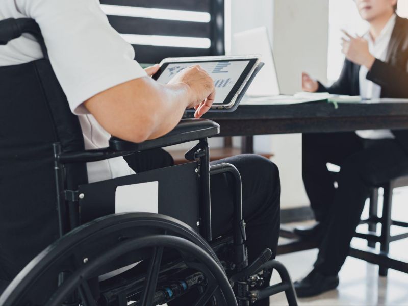 Person in a wheelchair using a tablet during a business meeting with a colleague at a desk.