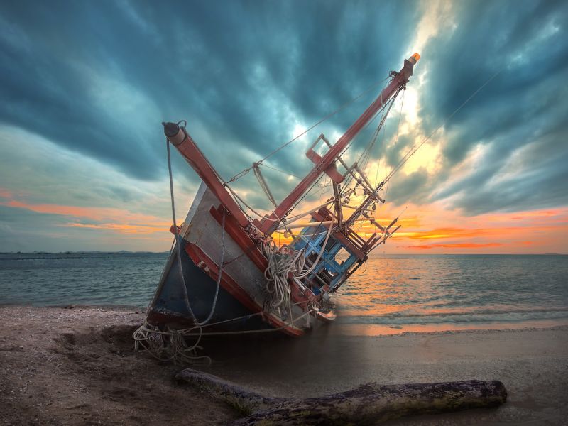 an old useless fishing boat laying dead on the sea beach at sunset scenery in background