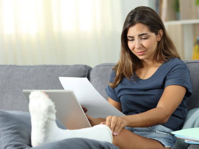 Woman with a leg cast sitting on a sofa, reading a document, looking concerned.