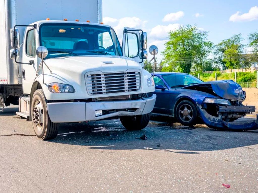 Truck and car collision on a sunny day, with visible front-end damage on the car.