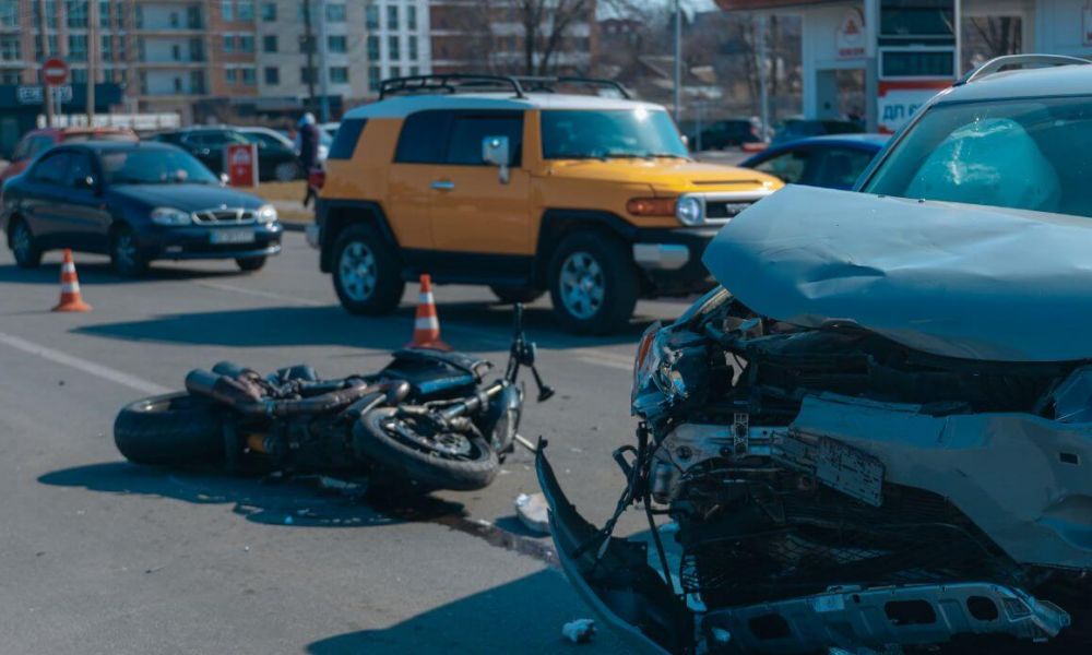 Traffic accident scene with a damaged car and a motorcycle, surrounded by traffic cones, in an urban area.