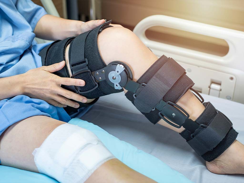 Patient in hospital bed with knee brace and bandages, recovering from surgery.