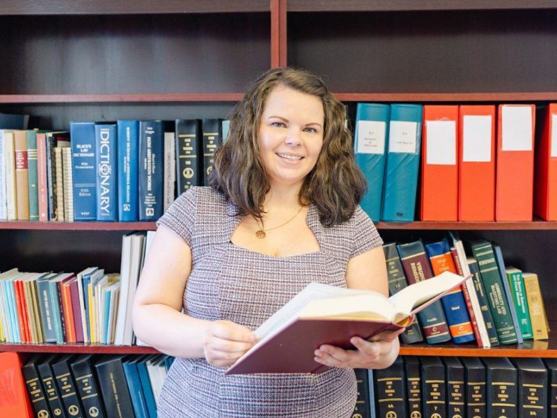 family law attorney Samantha Bull standing in front of a bookshelf smiling while holding an open book