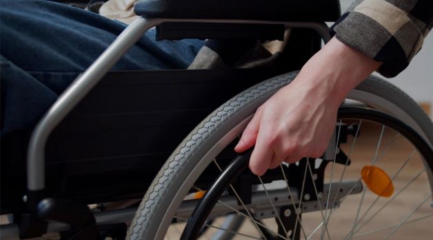 Person using a wheelchair indoors, gripping the wheel rim for mobility and support.