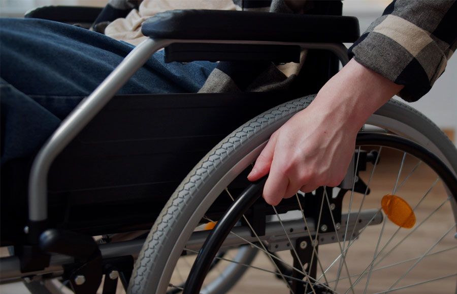 Person using a wheelchair indoors, gripping the wheel rim for mobility and support.