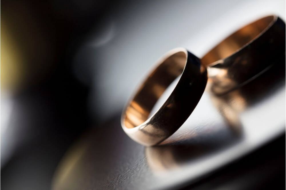 Two wedding rings lie overlapping on a reflective surface, with a soft-focus background creating a romantic and intimate atmosphere.