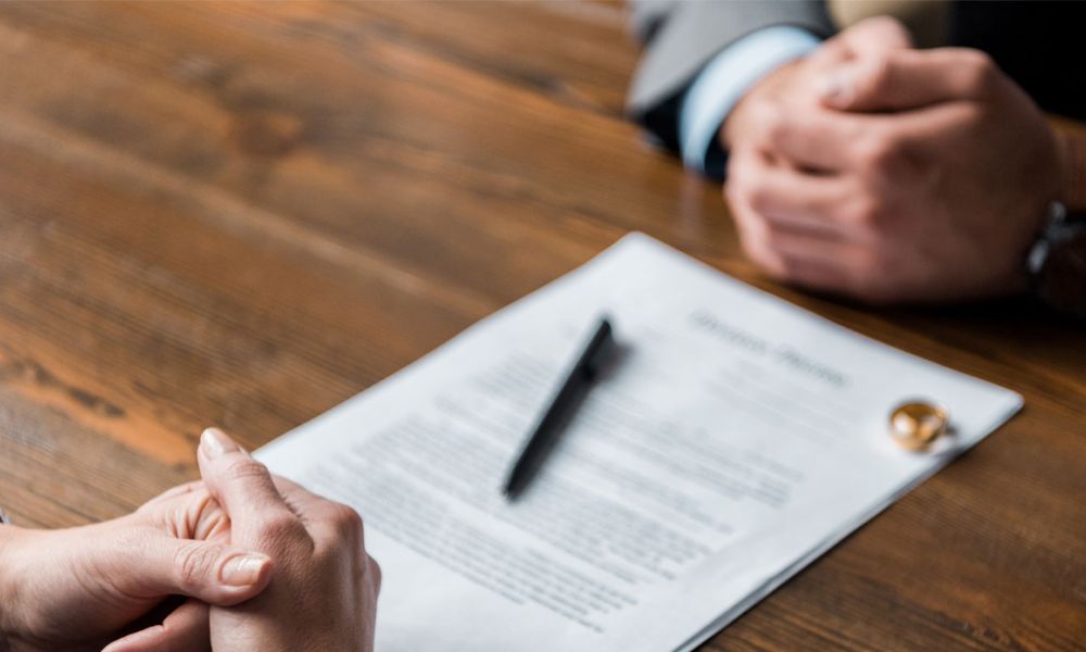 partial view of lawyer and client sitting at table with divorce decree and wedding rings