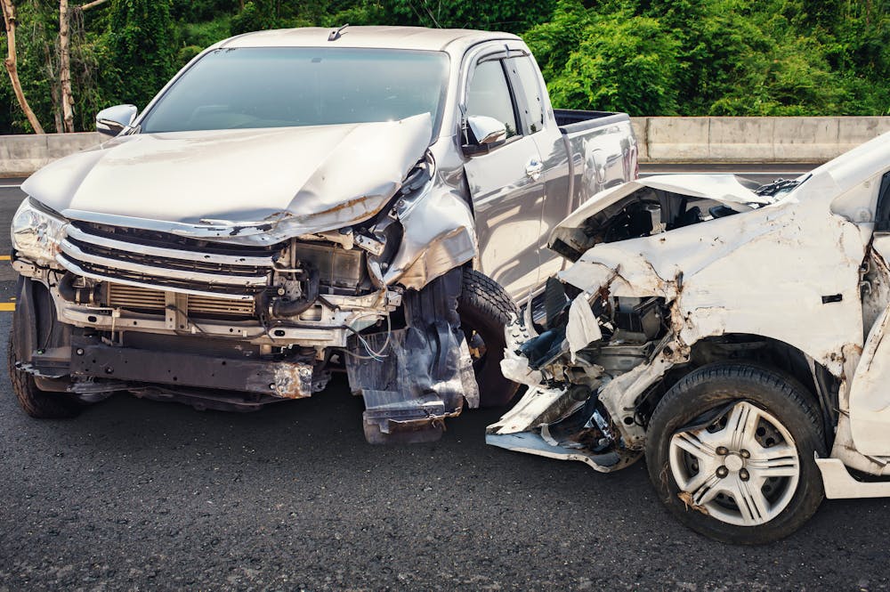 Two heavily damaged cars after a frontal collision on a highway with visible greenery in the background.