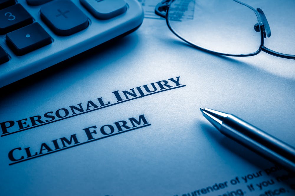a form that reads personal injury claim form with a pen and glasses laying on a table.