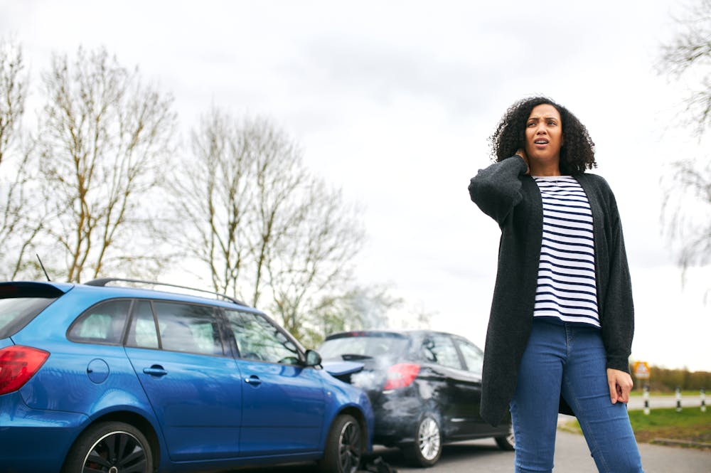 Woman holding her neck after exiting her vehicle due to a car accident