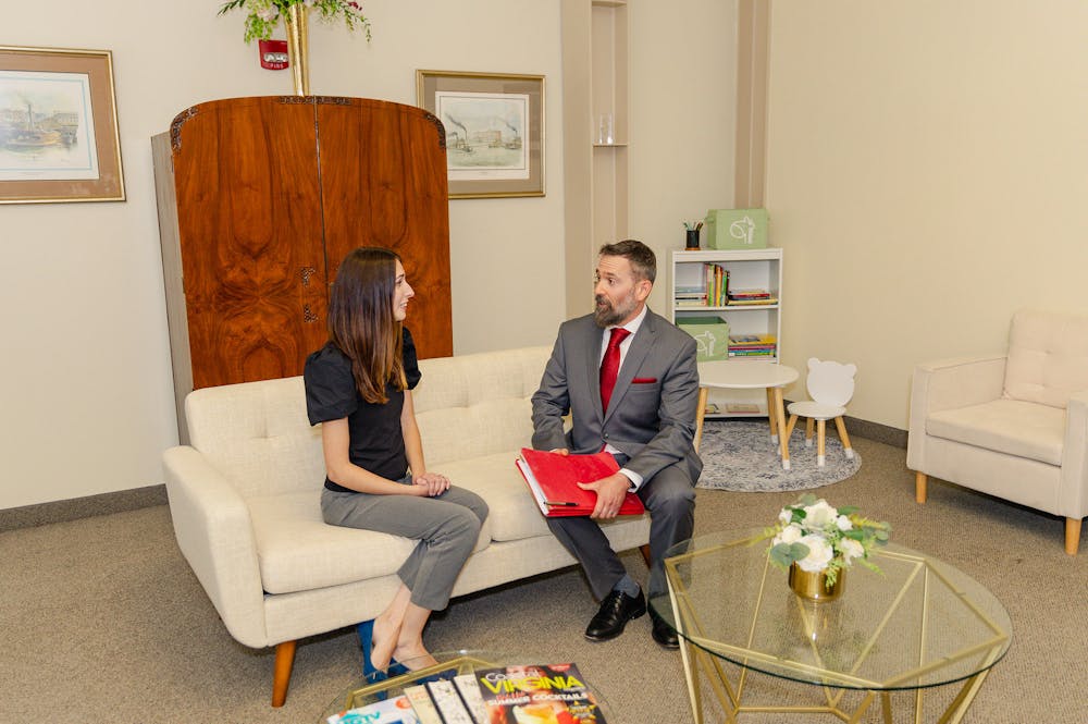 Two professionals having a conversation on a couch in a neatly decorated office space.