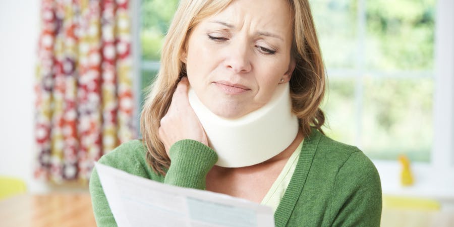 Woman with neck brace reading a document, expressing concern indoors.