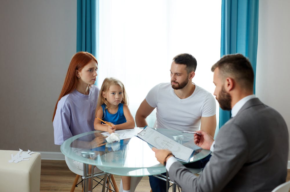 Family discussing paperwork with advisor at table in bright room.