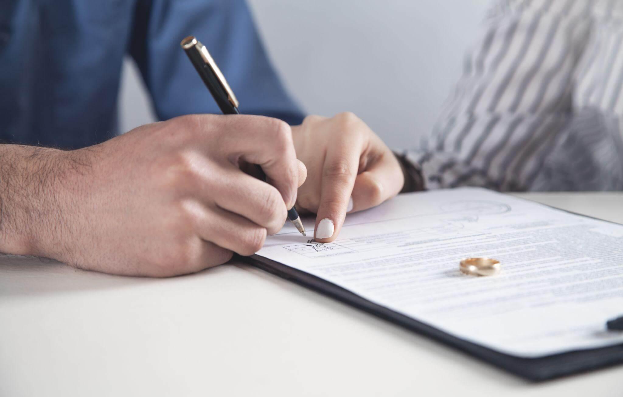 a person writing on a piece of paper with a pen, there's a wedding ring on top of it