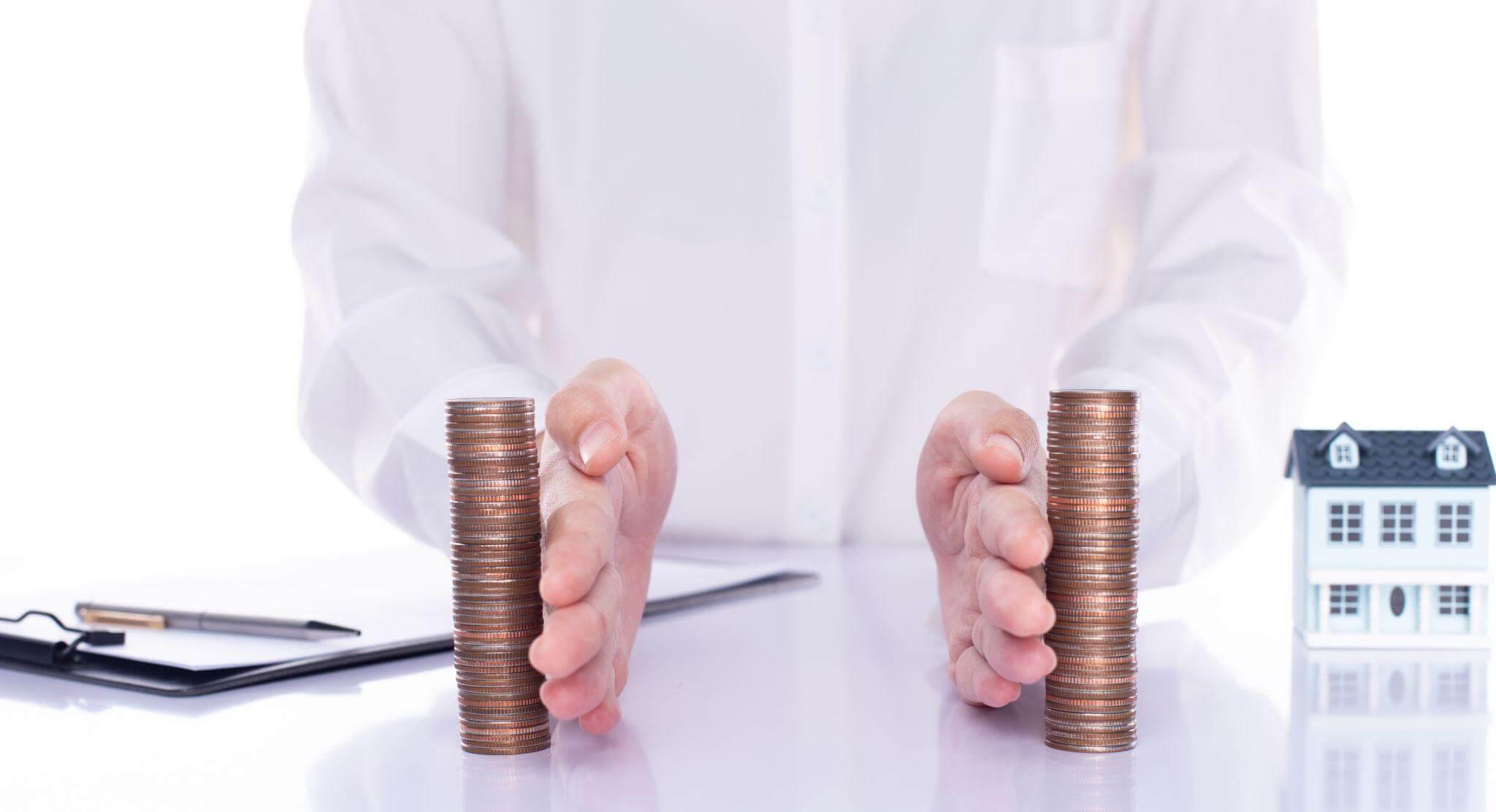 Person holding stacks of coins in front of a house, symbolizing financial implications in family law