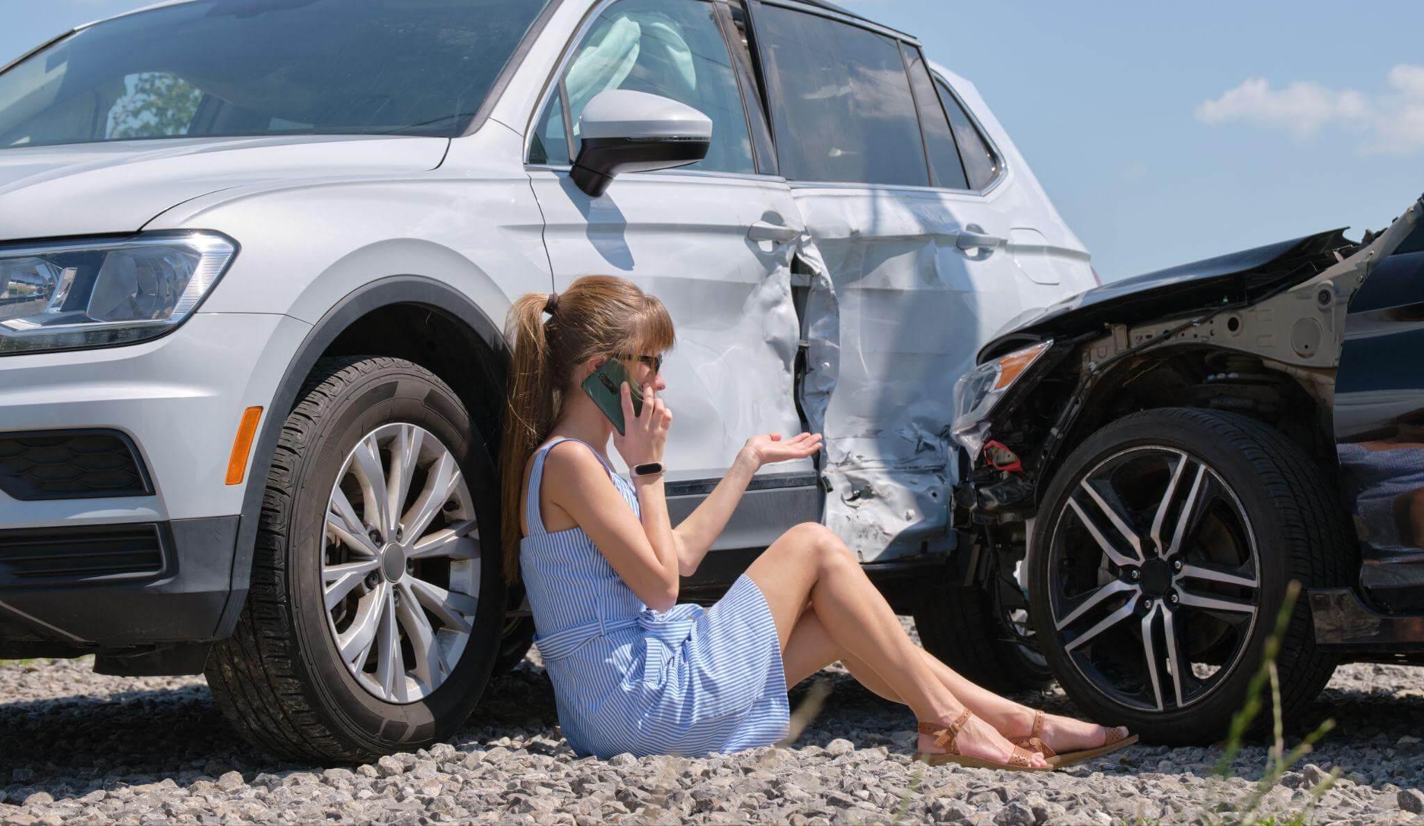 a woman sitting on the ground next to a car talking on a cell phone
