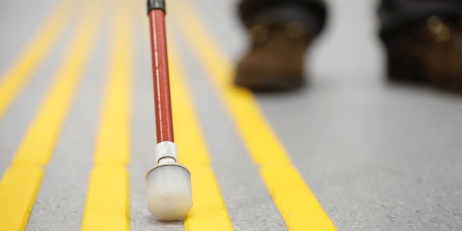 white mobility cane touching ground with yellow lines painted.