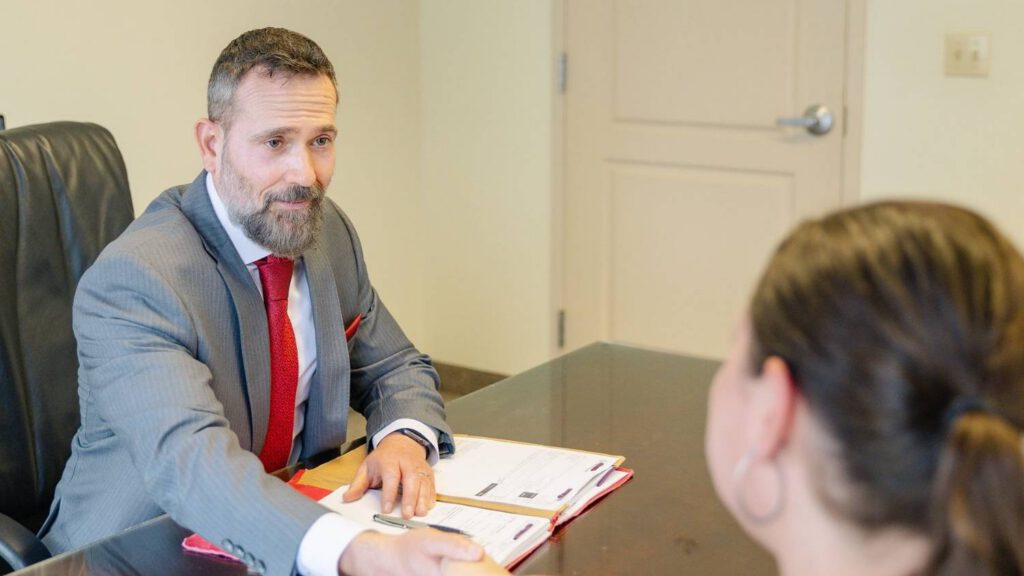 Jon Montagna personal injury lawyer shakes the hand of a client as they sit in front of a desk