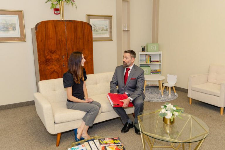 Two professionals having a conversation on a couch in a neatly decorated office space.