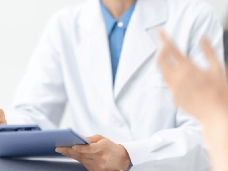 doctor writing on paper while talking to person in foreground