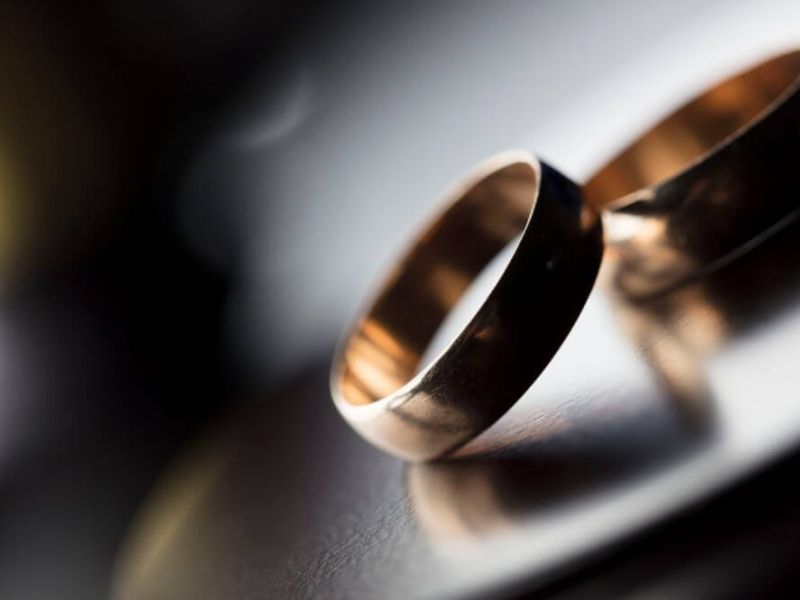 Two wedding rings lie overlapping on a reflective surface, with a soft-focus background creating a romantic and intimate atmosphere.