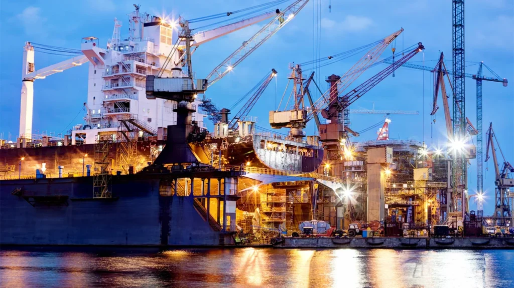 Shipyard cranes and a ship in dry dock in Newport News at dusk