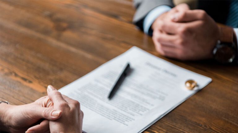 partial view of lawyer and client sitting at table with divorce decree and wedding rings